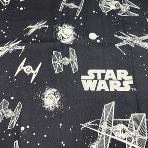May include: Black fabric with a white repeating pattern of Star Wars spaceships and the words "STAR WARS" with a trademark symbol.