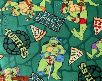 May include: Green fabric with a repeating pattern of Teenage Mutant Ninja Turtles characters, pizza slices, and the words "Turtle Power" and "Turtles".