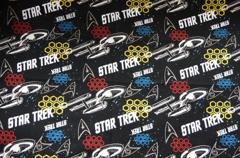 K&ouml;nnte beinhalten: Schwarzer Stoff mit einem sich wiederholenden Muster aus dem Star Trek-Logo, einem Raumschiff und Wabenformen in Rot, Gelb und Blau.
