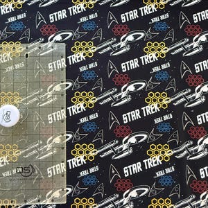 K&ouml;nnte beinhalten: Schwarzer Stoff mit einem sich wiederholenden Muster aus wei&szlig;en Star Trek Raumschiffen, gelben Wabenformen und dem Text "STAR TREK".