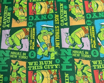 May include: Green fabric with a repeating pattern of Teenage Mutant Ninja Turtles characters and phrases. The fabric features the words "We Run This City!" and "Catchin' a Cab!" in a comic book style font.