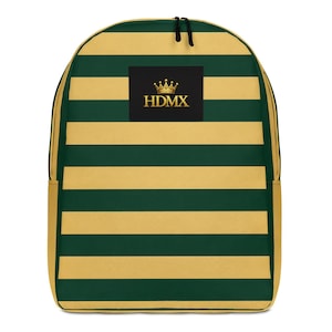 Puede incluir: Una mochila con rayas horizontales en verde oscuro y beige. Centrado en la parte frontal hay un parche rectangular negro que muestra un icono de corona dorada sobre el texto HDMX en fuente serif. La bolsa tiene un cierre de cremallera superior.