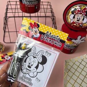 May include: A party favor bag with a Minnie Mouse coloring page and two crayons. The bag has a red, yellow, and white Minnie Mouse design with the text "Maria Victoria" on it.