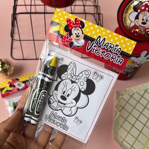 May include: A clear plastic bag filled with two yellow and black crayons and a coloring page featuring a black and white illustration of Minnie Mouse. The coloring page has the text "Maria Victoria" at the bottom.