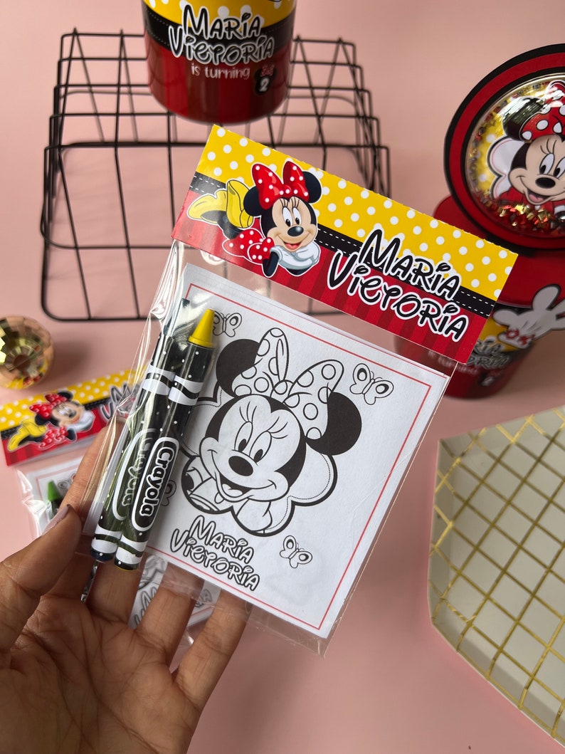 May include: A clear plastic bag filled with two yellow and black crayons and a coloring page featuring a black and white illustration of Minnie Mouse. The coloring page has the text "Maria Victoria" at the bottom.