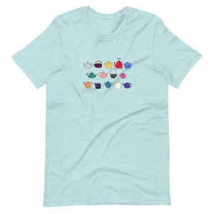 Può includere: Una maglietta blu chiaro con un design di 15 teiere di diversi colori. Le teiere sono tutte di forme e dimensioni diverse.
