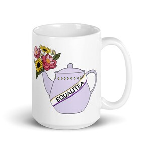 Può includere: Tazza in ceramica bianca con una teiera viola con un nastro giallo, viola e bianco che dice "EQUALITEA" e un mazzo di fiori che escono dal beccuccio.