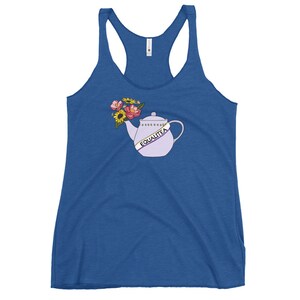 Può includere: Una canotta blu con una teiera viola con un nastro che dice "Equalitea" e fiori che escono dal beccuccio.