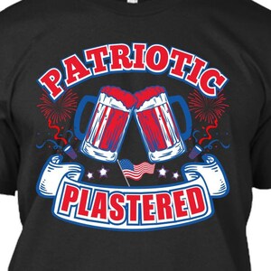 Puede incluir: Camiseta negra con un gráfico rojo, blanco y azul de dos jarras de cerveza chocando, fuegos artificiales y el texto "PATRIOTIC PLASTERED".