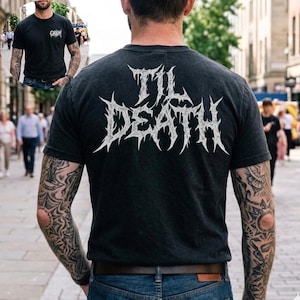 May include: Black t-shirt with the text "TIL DEATH" in a white, spiky font on the back. The shirt also features a small logo on the front. The image shows a person wearing the shirt, with visible tattoos on their arms.