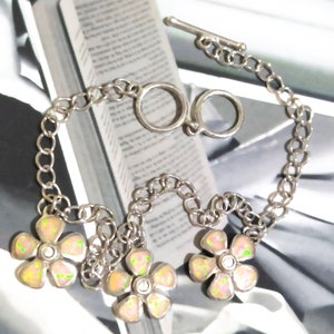 May include: A silver chain bracelet with three pink opal flower charms. Each flower has a small clear rhinestone in the center.