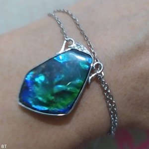 May include: A silver chain necklace with a large iridescent green and blue gemstone pendant.