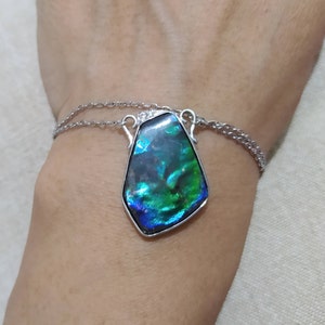 May include: A silver chain necklace with a large iridescent green and blue gemstone pendant.