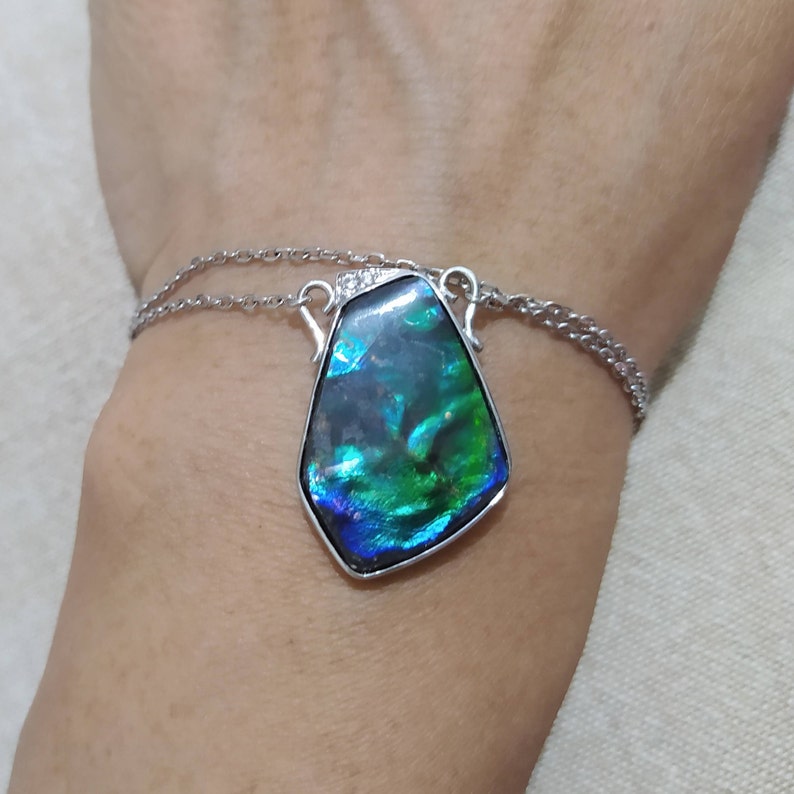 May include: A silver chain necklace with a large iridescent green and blue gemstone pendant.