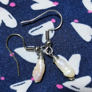 May include: A pair of silver earrings with white pearl-like drops. The earrings have a simple design and are perfect for everyday wear.