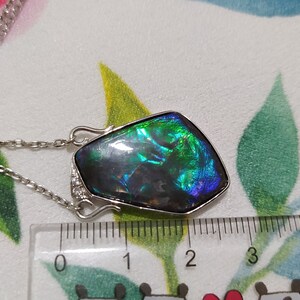 May include: A silver chain necklace with a large iridescent green, blue, and black gemstone pendant. The pendant is approximately 2.5 inches long and is set in a silver frame.