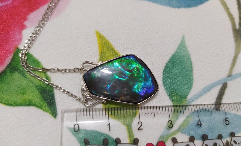 May include: A silver chain necklace with a large iridescent green, blue, and black gemstone pendant. The pendant is approximately 2.5 inches long and is set in a silver frame.