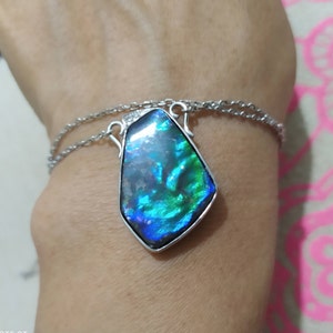 May include: A silver chain necklace with a large iridescent blue and green gemstone pendant. The pendant is shaped like a teardrop and has a faceted surface.