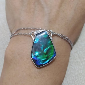 May include: A silver chain necklace with a large iridescent green and blue gemstone pendant.