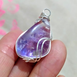 May include: A purple amethyst gemstone pendant wrapped in silver wire. The pendant has a teardrop shape and is set in a simple wire frame.