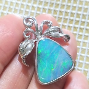 Op de afbeelding: Een zilveren hanger met een driehoekige blauwe opaal-edelsteen gezet in een bloemmotief.