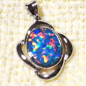 Può includere: Un ciondolo d'argento con una pietra di opale blu incastonata in una cornice ovale d'argento. L'opale presenta riflessi iridescenti di rosso, verde e giallo.