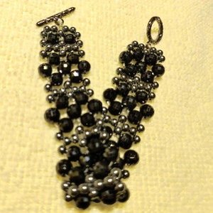 May include: A black and silver beaded bracelet with a toggle clasp. The bracelet is made with small round beads and has a layered design.