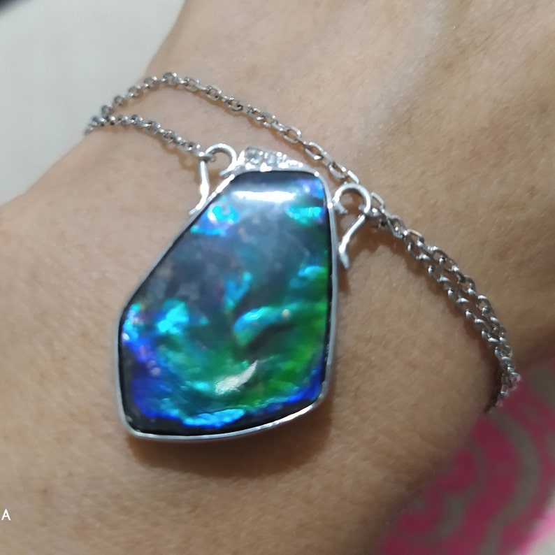 May include: A silver chain necklace with a large, iridescent, teardrop-shaped pendant. The pendant has a blue, green, and purple color scheme.