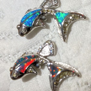 May include: Two silver fish pendants with opal inlay. One fish has a blue and green opal, the other has a red and black opal.