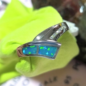May include: A silver ring with a blue and green opal stone set in a curved band. The ring is accented with small clear stones.
