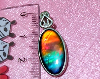 May include: A silver pendant with a large oval-shaped iridescent gemstone. The gemstone has a rainbow of colors, including red, orange, yellow, green, blue, and purple. The pendant is about 1 inch in length.