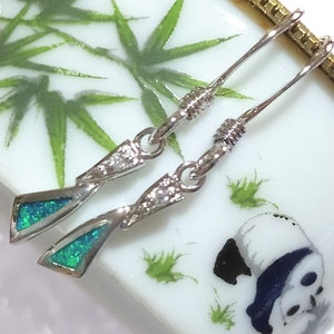 May include: A pair of silver dangle earrings featuring a teardrop-shaped blue opal stone and clear cubic zirconia accents.