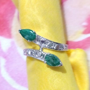 Op de afbeelding: Een zilveren ring met twee groene edelsteen accenten. De ring is ontworpen in de vorm van een slang met de edelstenen in de kop van de slang.