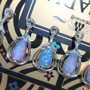 May include: Five silver pendants featuring opal stones. Each pendant has a teardrop-shaped opal stone set in a silver frame with intricate details. The opals are iridescent with shades of blue, green, and pink.