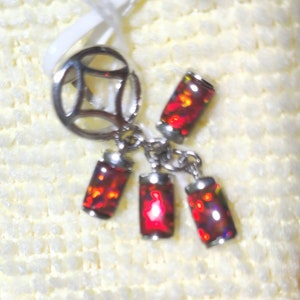 May include: A silver charm with a circle design and four dangling red opal stones.