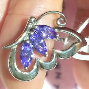 Könnte beinhalten: Ein silberner Schmetterlingsanhänger mit violetten Amethyststeinen.