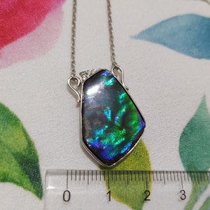 May include: A silver necklace with a large iridescent green and blue gemstone pendant. The pendant is about 2 inches long and has a geometric shape.