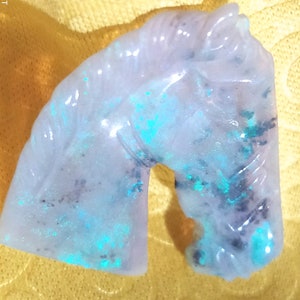 Puede incluir: Una figurita de caballo de color lila claro con motas iridiscentes azules y negras en toda la piedra.