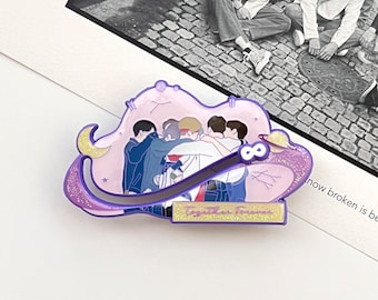 May include: A purple enamel pin featuring a group of seven figures in a circular embrace. The design includes a crescent moon, a planet with rings, and a gold rectangular plaque at the bottom with the text Together Forever in purple script.