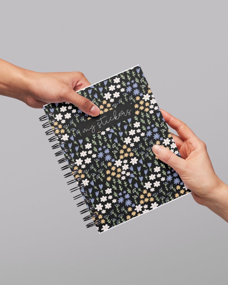 May include: A black spiral bound notebook with a floral pattern in shades of blue, yellow, and white. The notebook has the text "my stickers" written on the front.