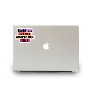 May include: A laptop computer with a sticker that reads "Hold on let me overthink this" in a colourful, retro font.