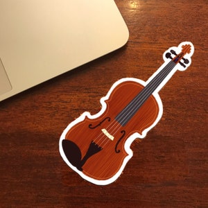 May include: A brown violin sticker with a white outline. The sticker is on a wooden surface.
