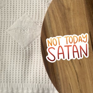 Peut inclure: Un plateau de service en bois avec un autocollant blanc qui dit "Not Today Satan" en lettres rouges et orange.