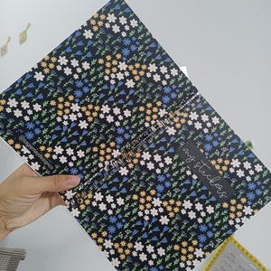 May include: A black spiral bound notebook with a floral pattern featuring white, blue, yellow, and green flowers. The text "my stickers" is written in white on a black rectangle on the cover.