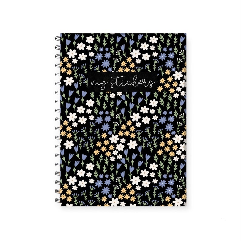 May include: A black spiral bound notebook with a floral pattern featuring white, yellow, and blue flowers. The notebook has a black label with the text "my stickers" written in white.