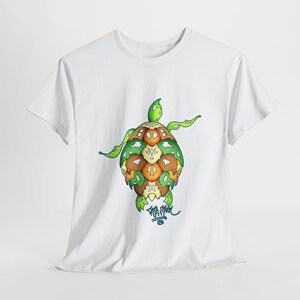 Puede incluir: Camiseta blanca con un gráfico verde, marrón y amarillo de una tortuga con una firma "SHAYMAN" debajo.