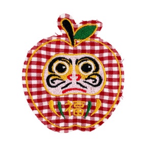 May include: Red and white gingham fabric apple with an embroidered daruma doll face and the word "福" (meaning "good fortune") in gold thread.