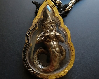Könnte beinhalten: Eine goldene Halskette mit einem Anhänger aus klarem Glas, der ein silberfarbenes Naga zeigt, eine mythische schlangenartige Kreatur mit einem menschenähnlichen Kopf und Oberkörper.