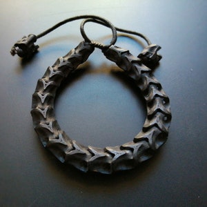 Peut inclure: Un bracelet noir composé d'une série de formes géométriques imbriquées. Le bracelet est réglable avec un cordon noir et deux boutons noirs.
