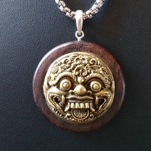 May include: A silver chain necklace with a round wooden pendant featuring a gold-coloured, detailed, mythical creature face.